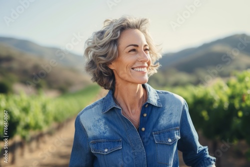 Portrait of a happy woman in her 60s sporting a versatile denim shirt in backdrop of rolling vineyards © Markus Schröder