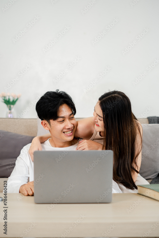 Young couple shares a playful moment with a laptop on a comfortable sofa, creating a lighthearted and loving atmosphere. Young couple shares a playful moment with a laptop on a comfortable sofa, creating a lighthearted and loving atmosphere.