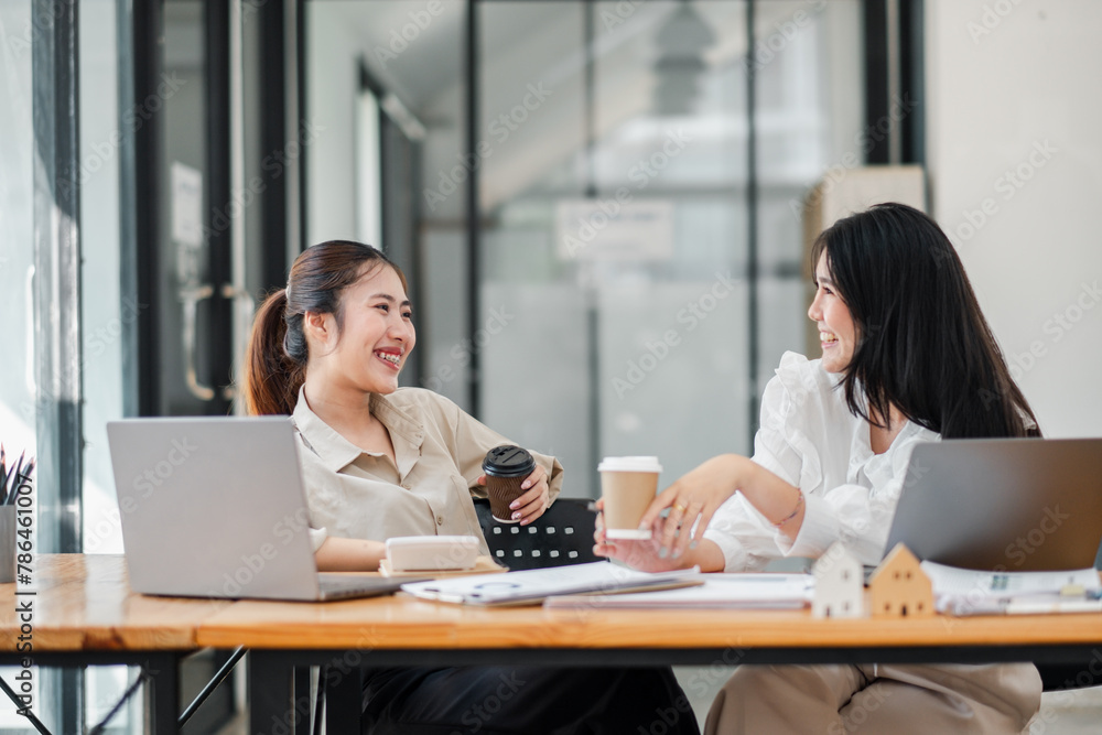 Two female colleagues share a light-hearted moment with coffee during a casual office meeting. Two female colleagues share a light-hearted moment with coffee during a casual office meeting.