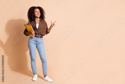 Full size photo of cheerful woman dressed brown shirt hold copybook look directing at sale empty space isolated on beige color background © deagreez
