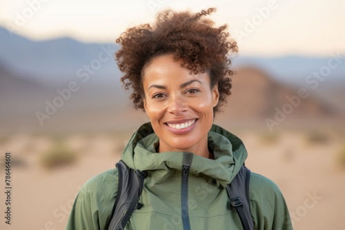 Portrait of a grinning afro-american woman in her 40s wearing a lightweight packable anorak on backdrop of desert dunes