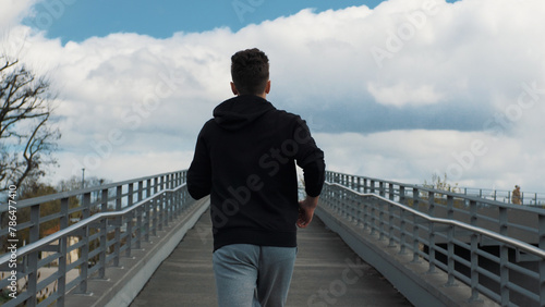 A young man runs forward. The camera is behind the man. Movement towards the goal. Motivation. Running on an asphalt bridge
