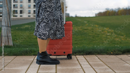 Close-up of the woman's legs stand still with the red suitcase. The beginning of the journey
