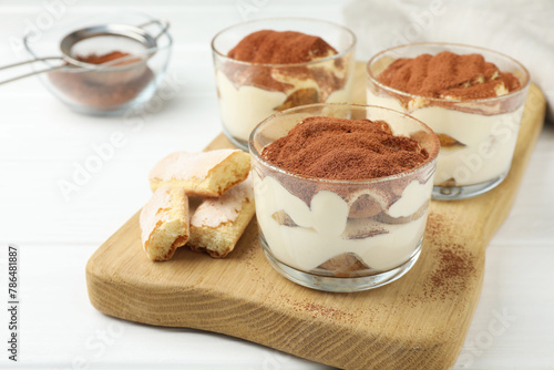 Delicious tiramisu in glasses and cookies on white table