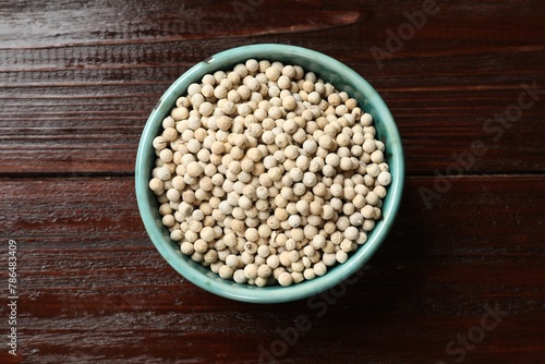Aromatic spice. White pepper in bowl on wooden table, top view