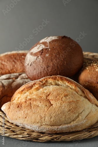 Wicker basket with different types of fresh bread on grey table, closeup