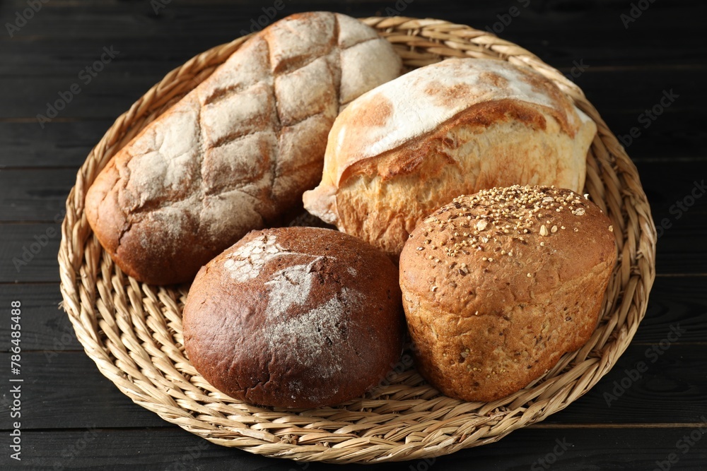 Wicker basket with different types of fresh bread on black wooden table