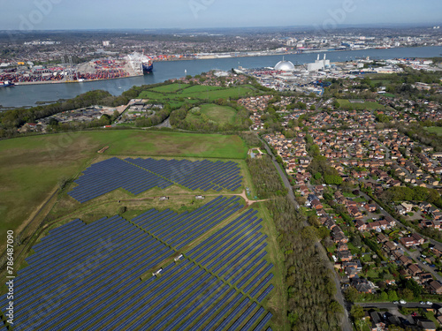 Road and green belt dividing Marchwood residential area with houses and field with large solar farm. Aerial view towards Southampton Docks and container terminal. Gas fired Power Station on the shore.