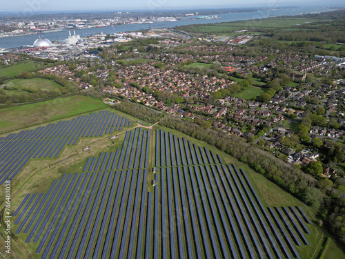 Aerial above large solar farm near Marchwood village. View on solar panels, residential area and industrial estate with Marchwood Power Station. Southampton city at distance and Solent coastline.
