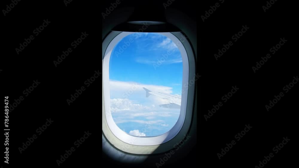 View of an airplane wing from a porthole against a blue sky background. A passenger plane flies above the clouds in the morning light. The concept of traveling by air. Fear of heights, aerophobia. 4K View of an airplane wing from a porthole against a blue sky background. A passenger plane flies above the clouds in the morning light. The concept of traveling by air. Fear of heights, aerophobia. 4K