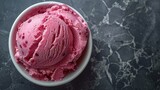   A marble countertop hosts a bowl brimming with pink ice cream, accompanied by a separate cup of the same treat