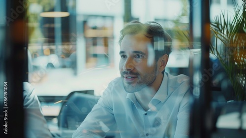 A cheerful manager leading a discussion with his team, seen through the transparent walls of the meeting room. 