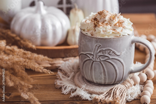 A seasonal drink. Delicious pumpkin latte with whipped cream and cinnamon in a mug on a wooden table in the living room interior.Autumn decor in the house. Scandinavian style.