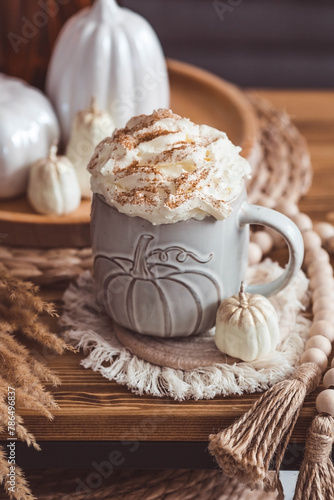 A seasonal drink. Delicious pumpkin latte with whipped cream and cinnamon in a mug on a wooden table in the living room interior.Autumn decor in the house. Scandinavian style.