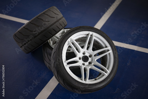 Fototapeta Naklejka Na Ścianę i Meble -  High definition and quality detail of three sports car wheels stacked on the parking lot floor, white 6-spoke wheels with Semislick tires