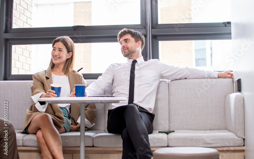 Two diverse smart businessman, woman wearing formal clothes, taking break, talking with relaxation, smiling with happiness, drinking coffee, sitting in indoor modern workplace. Business Concept.