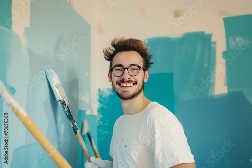 Cheerful man painting interior wall in blue color, new home  redecoration and renovation project photo