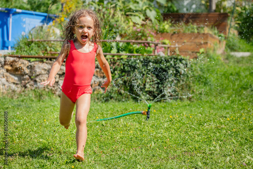 Screaming girl in red swimsuit running through sprinkler water