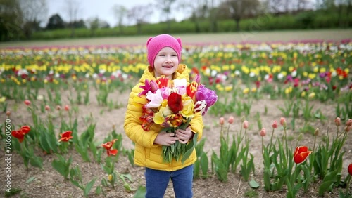 Adorable preschooler girl picking beautiful tulip flowers on farm. Outdoor summer activities for little kids.
