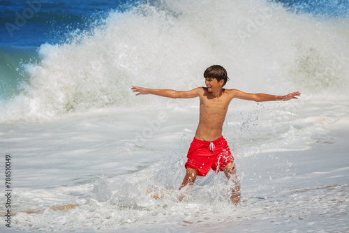 Boy, in red swim shorts with outstretched arms have fun at waves © Sergey Novikov