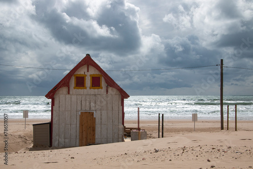Abandoned wooden house on a beach with the sea in the background and a cloudy blue sky