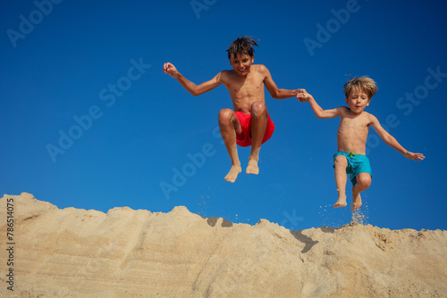 Pair of cheerful children jump from a sandbank against blue sky