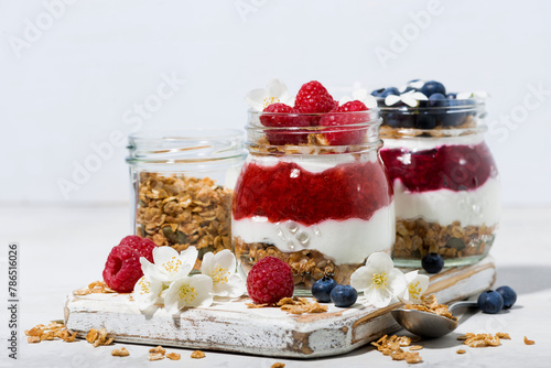 sweet desserts with granola, berry and fruit puree in jars on white wooden board, closeup