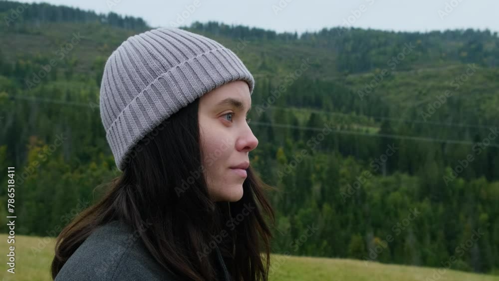 Portrait of beautiful young woman in mountains. Female traveler enjoys mountain forest landscape after climbing the hill on cloudy cold autumn day Portrait of beautiful young woman in mountains. Female traveler enjoys mountain forest landscape after climbing the hill on cloudy cold autumn day