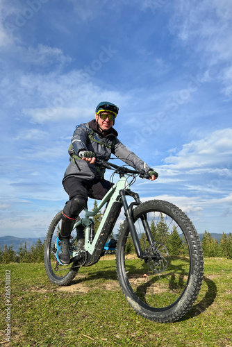 Cyclist man riding electric mountain bike outdoors. Male tourist biking along grassy trail in the mountains  wearing helmet and backpack. Concept of sport  active leisure and nature.