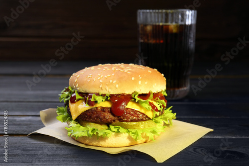 Burger with delicious patty and soda drink on black wooden table