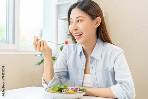 Diet concept, happy asian young woman hand use a fork to prick tomato, fresh vegetable or green salad, eat nutrition food  on table at home, low fat to good body. Girl getting weight loss for healthy.
