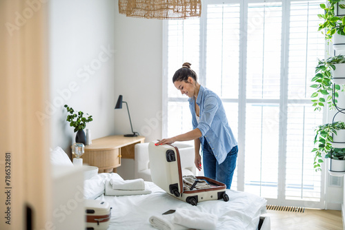 Young woman packing suitcase in the bedroom, preparing for travel
