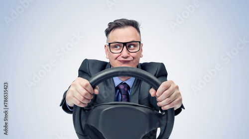 Portrait of a comical businessman in a dark suit and glasses holding a car steering wheel in his hands, on a light blue background