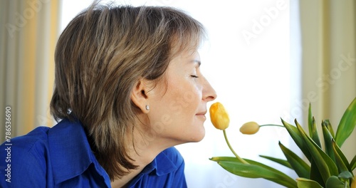 Middle-aged woman inhales yellow tulip scent. Flower fragrance, natural aromatherapy moment, Gen X. Flowers essence, peaceful woman. Flowers allure, tranquil experience, mature lady delight.