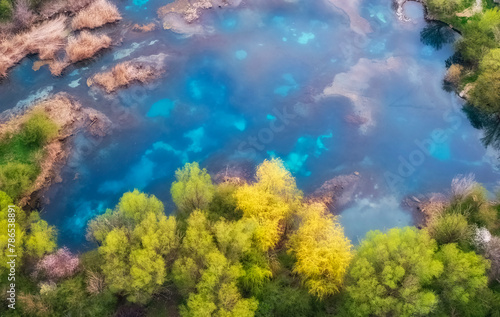 View from the air of the turquoise Lake Balykty, in the spring among green hills, and a blooming orchard near the Shymkent region of Kazakhstan.