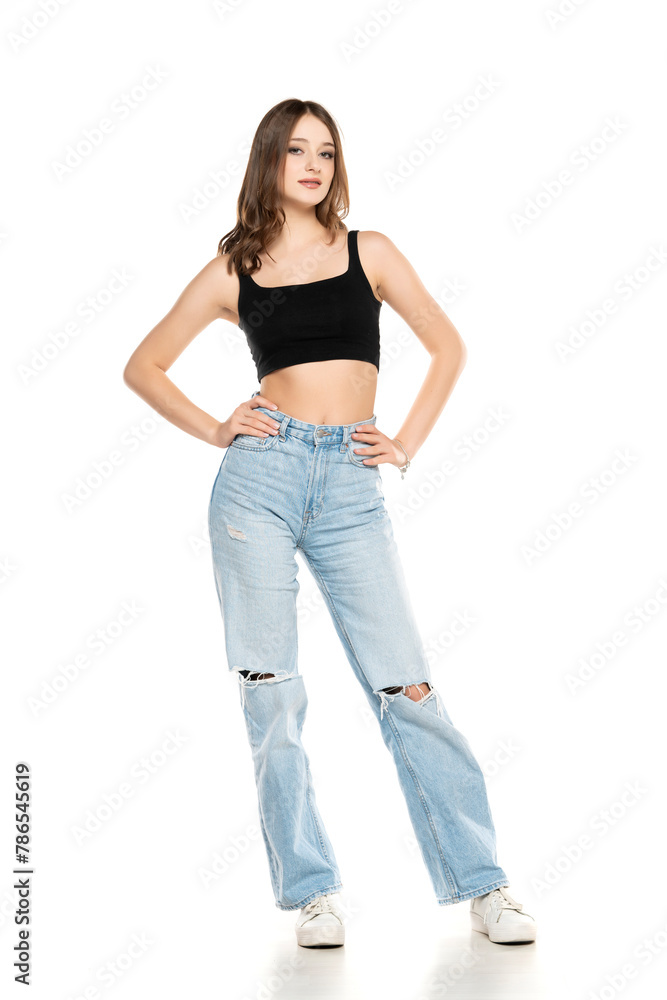 Young female model wearing ripped jeans and black sleeveless shirt posing on a white background. Front view