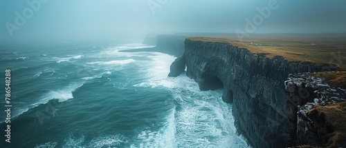 A rocky cliff overlooks the ocean with a misty, foggy atmosphere photo