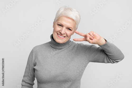 Playful senior woman with peace sign near eye photo