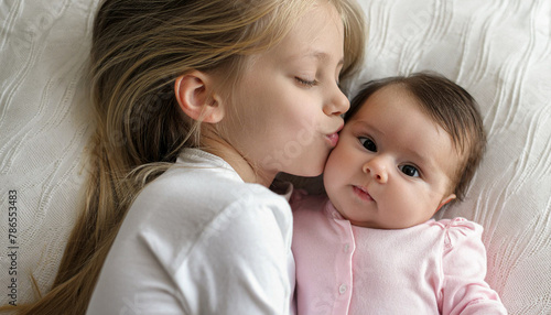 adorable child kissing little sister lying on white bedding