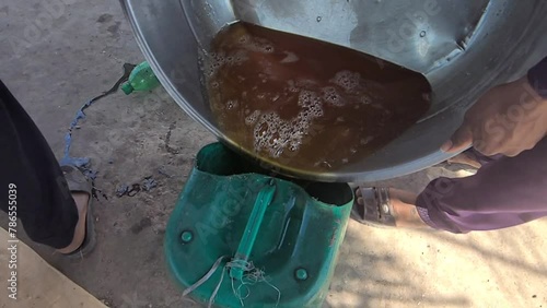 A man pours sugarcane juice into a plastic can after thickening it to make jaggery. Beautiful Slow Motion Footage. photo