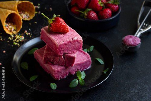 Strawberry ice cream, designed on a black round plate, with fresh strawberries