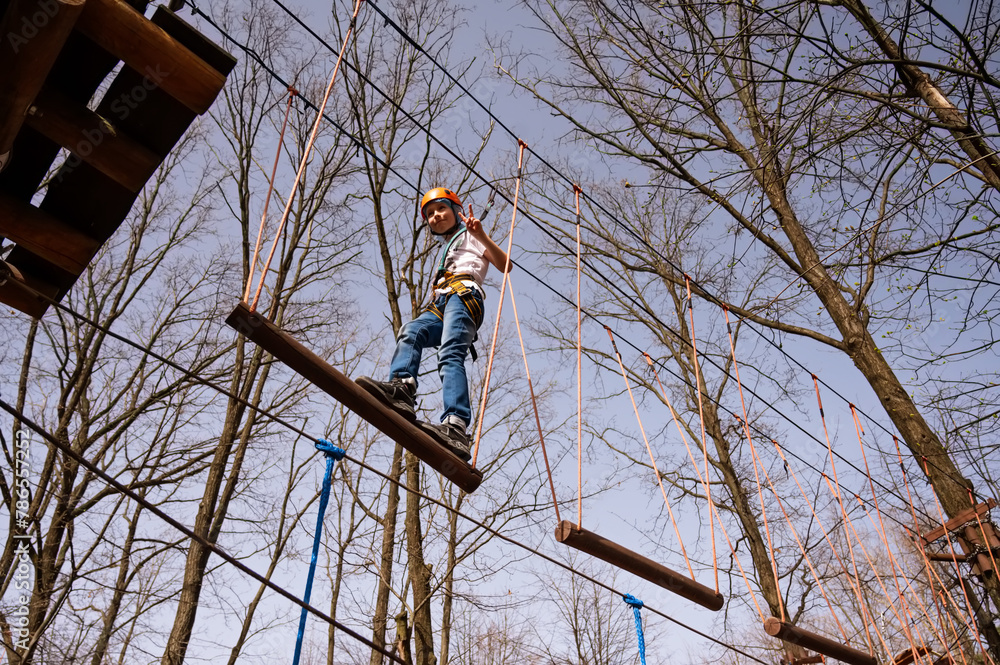 A boy in a helmet climbs a rope park in the spring