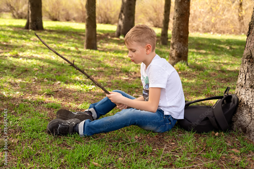 A boy with a stick sits on the grass in a spring park A boy with a stick sits on the grass in a spring park