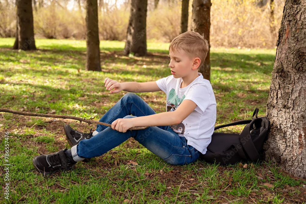 A boy with a stick sits on the grass in a spring park A boy with a stick sits on the grass in a spring park