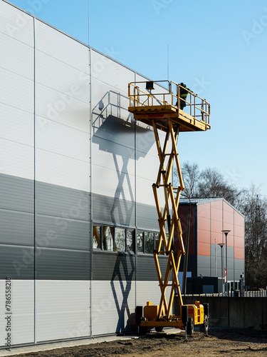 High elevated yellow self propelled scissor lift platform with worker for building wall inspection photo