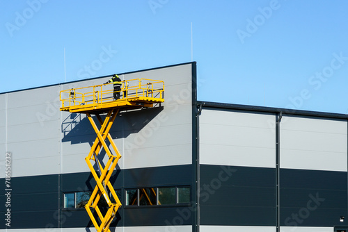 High elevated yellow self propelled scissor lift platform with worker for building wall inspection