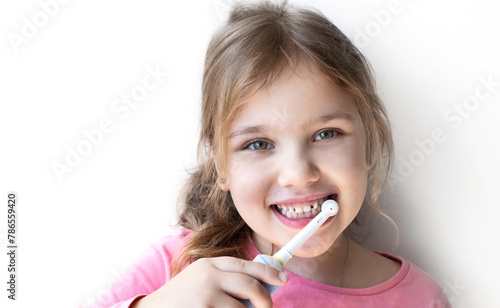 Beautiful blond girl cleaning her teeth with electric toothbrush on white background.Dental portrait.Smiling happy toddler. © nys