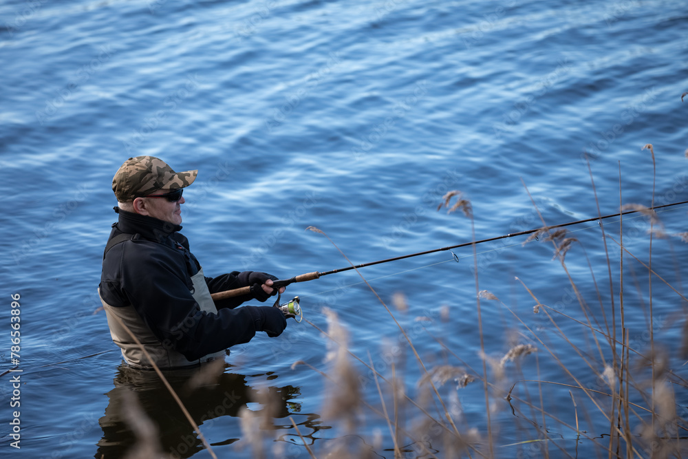 Fisherman in waders catches pike in the lake Fisherman in waders catches pike in the lake