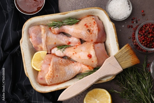 Flat lay composition with marinade and raw chicken drumsticks on brown table photo