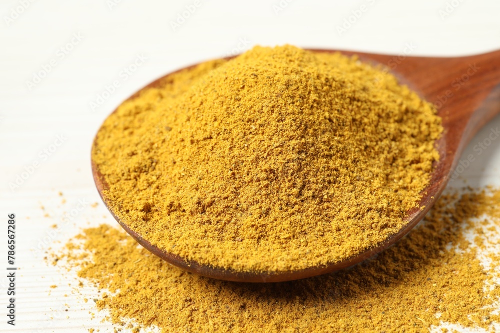 Curry powder in spoon on white wooden table, closeup Curry powder in spoon on white wooden table, closeup